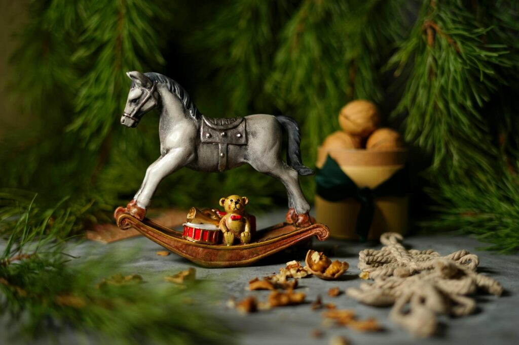 A charming rocking horse figurine with a teddy bear sits amidst winter greenery and walnuts, evoking holiday cheer.